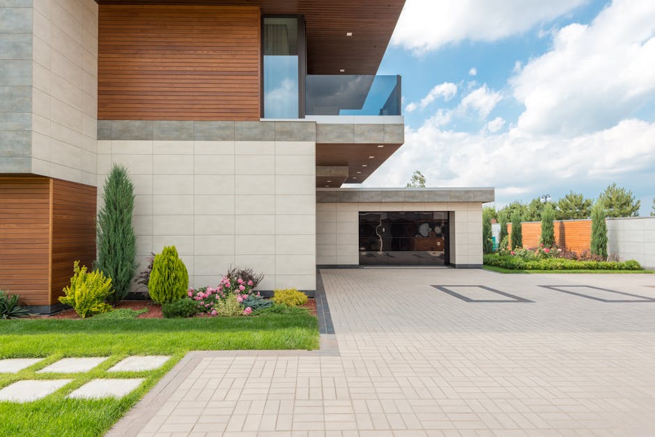 A modern minimalist house with a spacious driveway, landscaped garden, and clear blue sky.